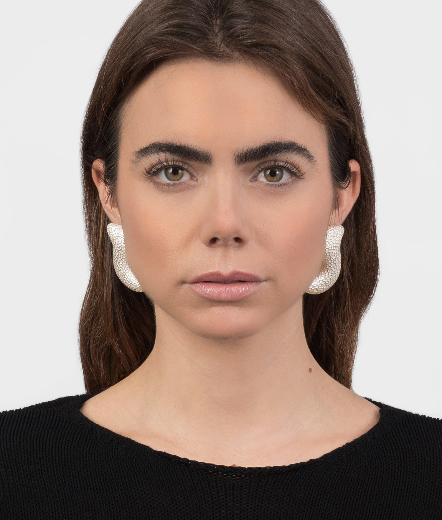 Mujer modelo vistiendo unos pendientes martillados y voluminosos de plata