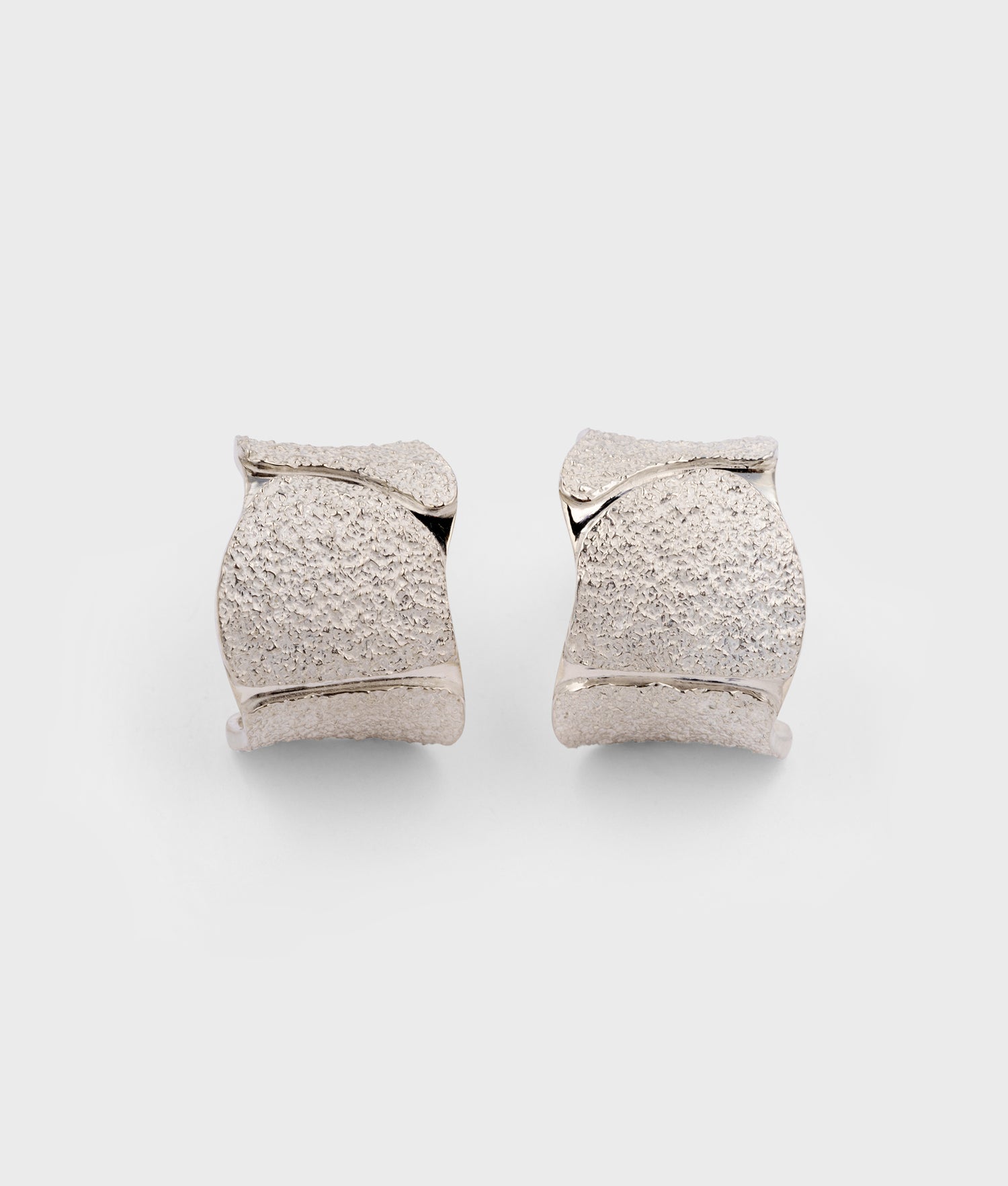 Pendientes exclusivos con un acabado que combina texturas terrosas y blanquecinas con dos canales en brillo espejo. Piezas fabricadas artesanalmente en Plata de Ley 925.